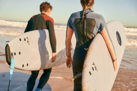 Back view of surfers with surfboards in wetsuit entering towards ocean for surfing on wavesの写真素材