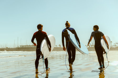 Back view of surfers with surfboards in wetsuit are walking on the beach after ride the wavesの写真素材