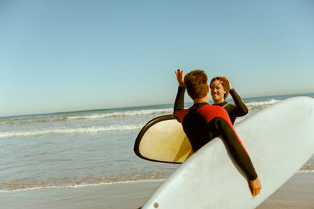 Surfer meets friend by waving hand while carrying surfboard on the beach