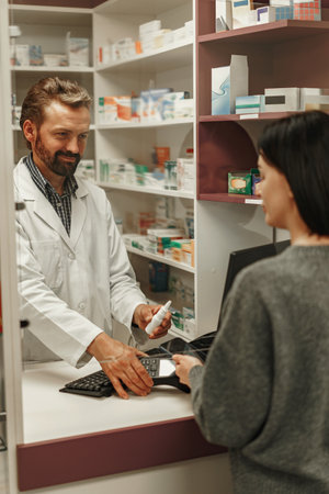 Smiling male pharmacist selling medications at drugstore to a woman customerの写真素材