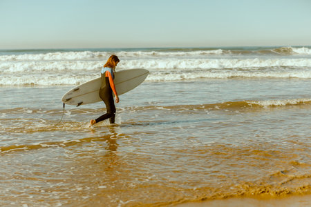 Female surfer in wetsuit with his surfboard entering out of sea after surfing on wavesの写真素材