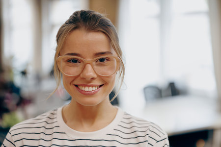 Portrait of young female manager in eyeglasses standing on office background and looks cameraの写真素材