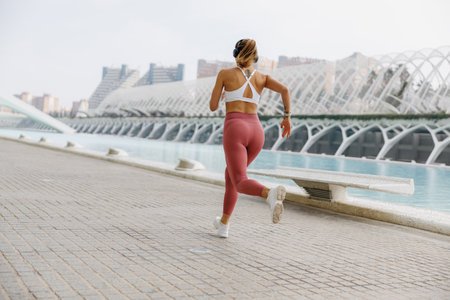 Back view of woman in sportswear is running on modern buildings background. Active lifestyle conceptの写真素材