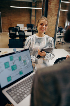 Smiling female business people standing in an office and using a laptop together