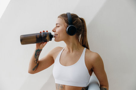 Young woman drinking water from a bottle after workout standing by a wall. High quality photoの写真素材