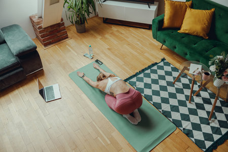 A woman is stretching on a yoga mat in living room with hardwood flooring. Home workout conceptの写真素材