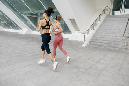 Two active women athlete running side by side along an outdoor track on modern buildings backgroundの写真素材