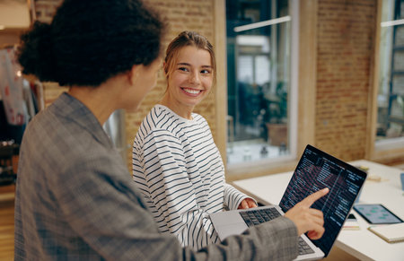 Female programmers enjoying time with laptop and distance job while standing at coworking space