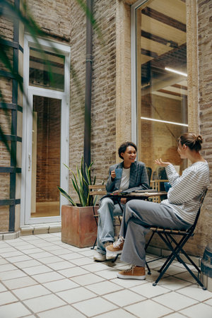 Two female colleagues have a coffee break time while sitting on office terraceの写真素材