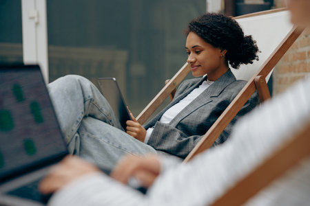 Smiling female freelancers sitting in coworking terrace while working on digital tablet and laptop