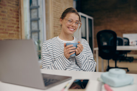 Young entrepreneur in eyeglasses working on laptop and drink coffee sitting in modern coworkingの写真素材