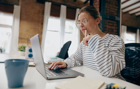 Pretty female freelancer working on laptop while sitting in modern coworkingの写真素材