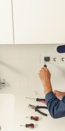 Professional handyman in uniform is fixing the electricity power socket on home kitchen
