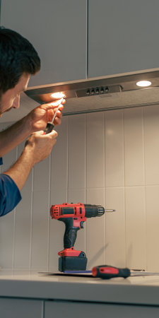 Professional male worker in uniform repairing modern cooker hood in kitchenの写真素材