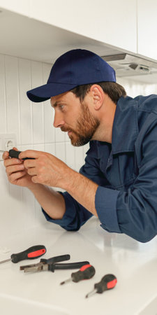Professional handyman in uniform is fixing the electricity power socket on home kitchenの写真素材