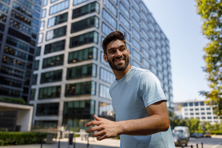 Smiling handsome man standing in modern big city on background of glass skyscrapers and looking away