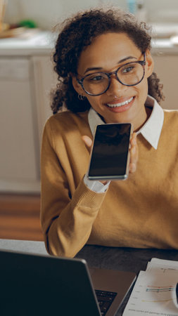 Female freelancer is record audio message on mobile phone while working on laptop from homeの写真素材