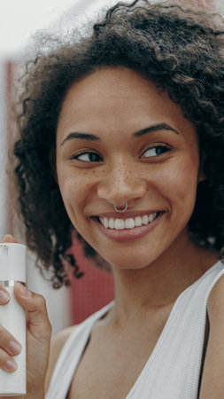 A Smiling Young Woman is Holding a Skincare Product While Enjoying the Outdoors Sunshineの写真素材