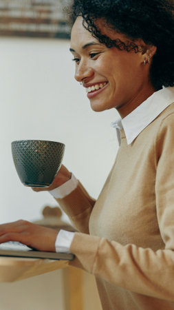 A woman is happily enjoying her coffee while focused on her tasks at a modern desk setupの写真素材