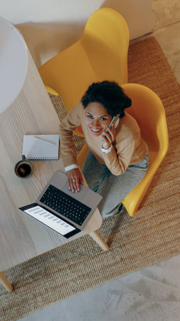 A woman is effectively working from home using her laptop while engaged in a phone call