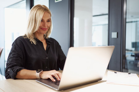 A Professional Woman Diligently Working on a Laptop in a Stylish Modern Office Spaceの写真素材