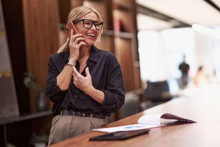 A cheerful, professional woman engaging in a lively phone conversation, showcasing her skillsの写真素材