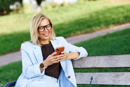 A stylish woman relaxes on a bench, enjoying her smartphone in her techfilled leisureの写真素材