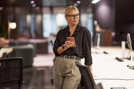 A modern office professional is actively using a smartphone within a contemporary workspace settingの写真素材