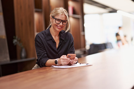A Professional Woman Actively Engages with Her Smartphone While in a Modern Workspaceの写真素材