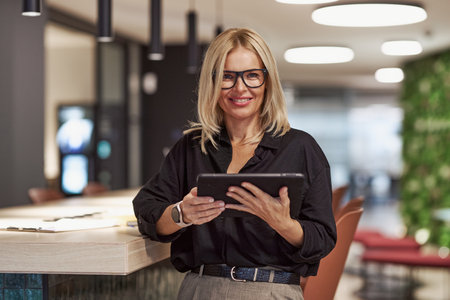 A Stylish and Confident Businesswoman is Using a Tablet Within a Modern Office Space Environmentの写真素材
