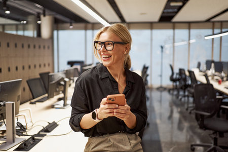 A cheerful professional uses a smartphone in a modern office with contemporary designの写真素材