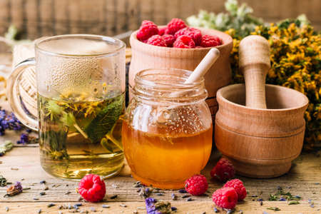 Herbal tea, honey and raspberries on a wooden table, alternative medicine, Ayurveda, dried flowers