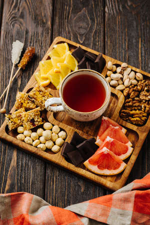 Menazhnitsa on a wooden background. Delicious tea, nuts and chocolate on a wooden square plateの写真素材