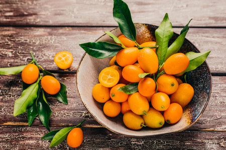 Fresh kumquat fruits with leaves in bowl on wooden backgroundの写真素材