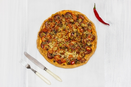 Pizza with salami and cherry tomatoes, with red chilli pepper and cutlery, on rusty white wood の写真素材