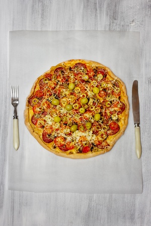Pizza with salami and cherry tomatoes, with red chilli pepper and cutlery, serving on rusty white wood の写真素材
