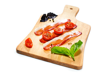 Dried cherry tomatoes with bacon served on carving board. Selective focus. Italian snack. Shallow depth of field. Isolated on white background.の写真素材