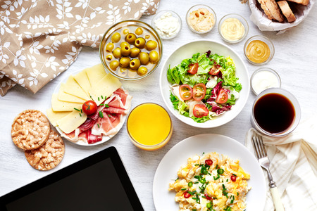 Fresh continental breakfast  Healthy food  Tablet, black screen  Scrambled eggs, salad, cheese, prosciutto, coffee and juice  Concept of business or holiday breakfast  Top view の写真素材