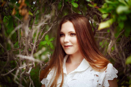 Beautiful smiling red-haired young woman, green park. Snowwhite style. White dress, summer.の写真素材