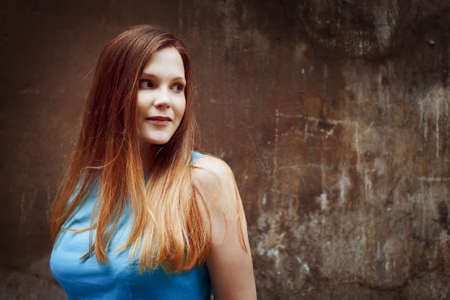 Beautiful red-haired young woman looking over her shoulder. City portrait, empty wall. の写真素材