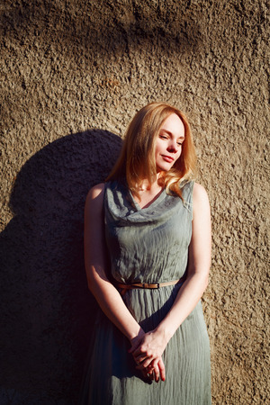 Fashion portrait of young attractive woman near grey wall. Blonde hair, sunset. Timeless style.の写真素材