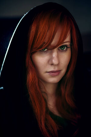Dramatic portrait of beautiful red hair woman in black hood. Grain added for better impression.の写真素材