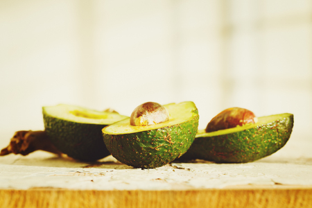 Fresh cut halves of avocado on wooden background. Image toned in warm green colors.
