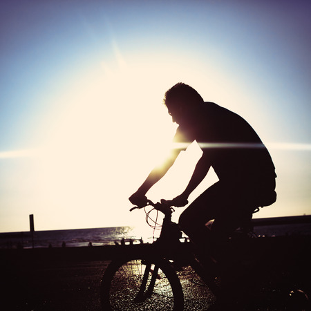 Man on bicycle riding at a coastline. Recreation concept. Silhouette image. Instagram color effect.の写真素材