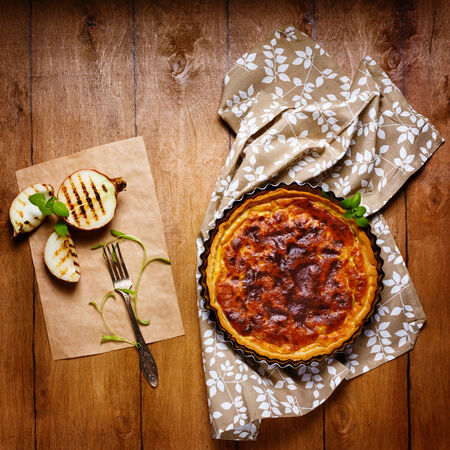 Onion pie or tart served with grilled halfs of onion and fresh herbs. Rustic style.の写真素材
