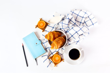 Breakfast with coffee and oranges and fresh baked tasty croissant on white background. Personal organizer with pencil for successful day.の写真素材