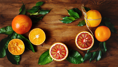 Orange fruit among green leaves on wooden table. Top view.
