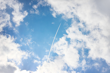 Airplane high in blue sky with cloudsの写真素材