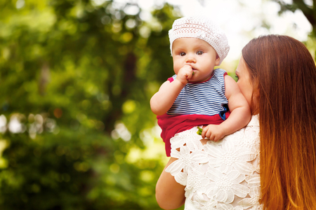 Cute Toddler Baby Girl sitting on Mom`s Hands, looking into camera. Relaxing in green summer Park.の写真素材