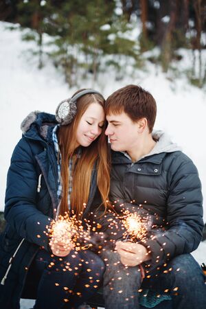 Happy Smiling Couple with Holiday Sparklers Celebrating Christmas Outdoors in Winter Forestの写真素材